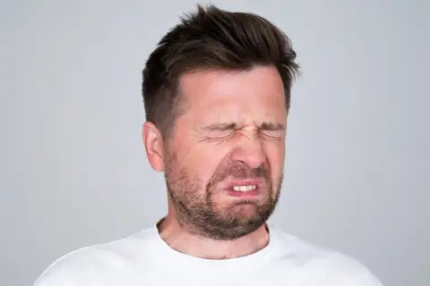 Mężczyzna z wykrzywioną twarzą, oczy zamknięte, czuje gorzki smak w ustach.