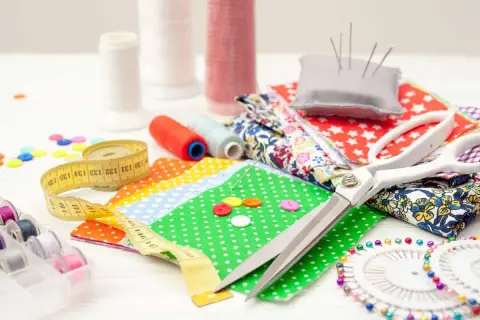 A collection of 10 sewing tools: scissors, measuring tape, spools of thread, needles, buttons, and fabric scraps, ready for a creative project.