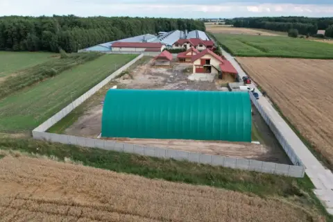 Zielona hala namiotowa na terenie gospodarstwa. Obok budynki mieszkalne i gospodarcze, otoczone polami uprawnymi. Grunty rolne zabudowane.