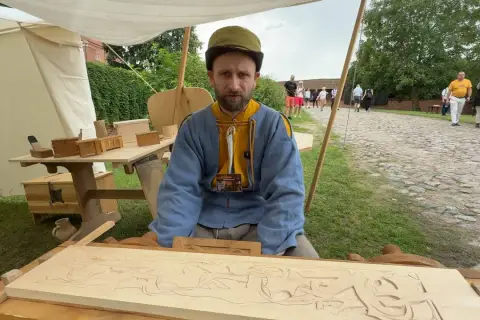 Snycerz co robi? Rzeźbi w drewnie, tworząc misterny wzór na desce.