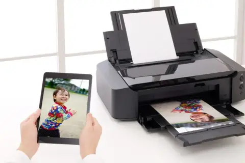 Uchwyć radość dziecka, drukując zdjęcia w domu. Tablet pokazuje uśmiechniętą twarz, a drukarka właśnie wydrukowała podobny kadr.