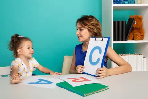 Nauczycielka pokazuje dziecku literę C, ucząc je, jak nauczyć dziecko głoskowania. Na stole litery A i R.