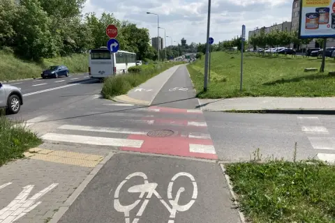 Przejście dla pieszych na ścieżce rowerowej, z oznaczeniem roweru. Autobus i samochody czekają na drodze.