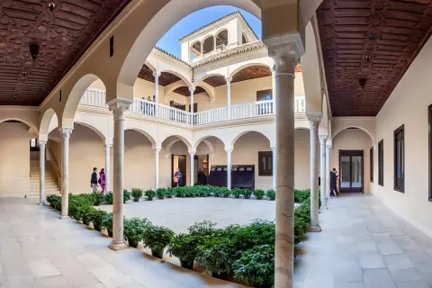 Wnętrze muzeum Picassa w Maladze, z dziedzińcem otoczonym arkadami, zdobionymi drewnianymi stropami i rzędami zieleni.