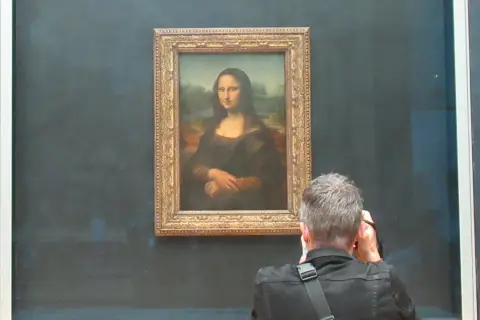 Ein Mann fotografiert die Mona Lisa. Die Frage, wie lange hat Da Vinci für die Mona Lisa gebraucht, beschäftigt viele Besucher.