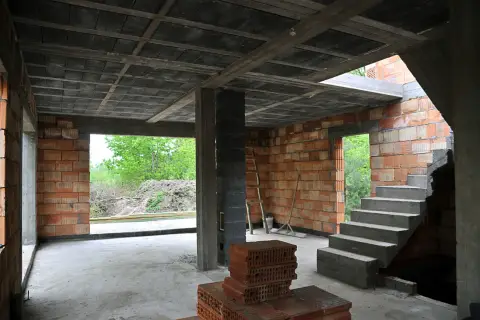 Wnętrze budowy z widocznymi stropy gęstożebrowe, betonowymi schodami i ceglanymi ścianami.