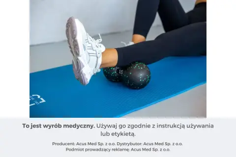 Kobieta wykonuje rolowanie mięśni łydki za pomocą czarnego rollera z zielonymi kropkami, leżąc na niebieskiej macie.