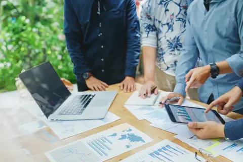 Team discute grafici e dati su un tavolo all'aperto, pianificando i loro buoni propositi per il futuro.