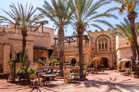 Sonniger Innenhof mit Palmen und traditioneller Architektur in der Agadir Altstadt. Tische und Stühle laden zum Verweilen ein.