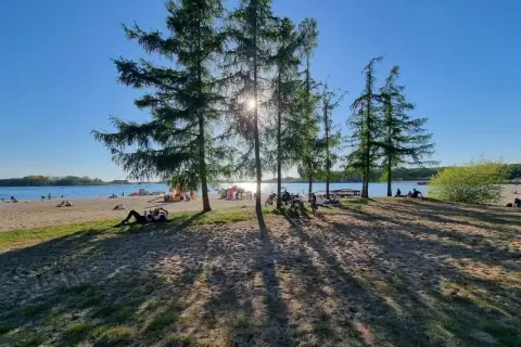 Słoneczny dzień nad jeziorem, ludzie odpoczywają na plaży, rowery czekają. Skorzęcin atrakcje to idealne miejsce na relaks.