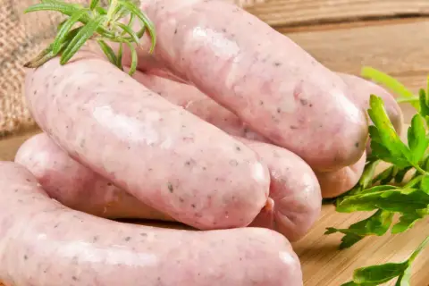Surowa biała kiełbasa na desce, z gałązką rozmarynu i natką pietruszki. Dowiedz się, ile gotować białą kiełbasę surową, by była idealna.