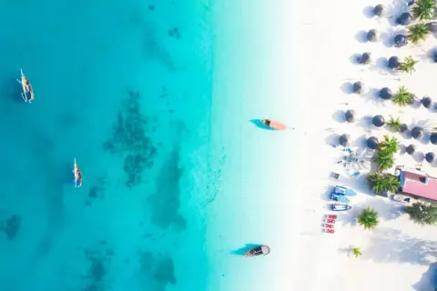 Rajska plaża na Zanzibarze, gdzie turkusowa woda i biały piasek tworzą idealne tło dla tradycyjnych łodzi. Można tu poczuć atmosferę wakacji, marząc o przygodach i wymieniając się wrażeniami, jakby to była lokalna waluta.
