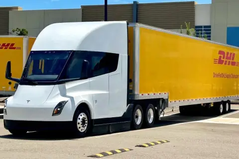Biała ciężarówka Tesla Semi z żółtą naczepą DHL stoi na parkingu.