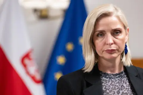 Znana posłanka KO zrezygnowała z mandatu dla kariery w biznesie prywatnym. Na zdjęciu kobieta z blond włosami, w czarnej marynarce, na tle flag Polski i UE.