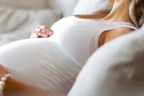Kobieta w ciąży odpoczywa na kanapie, delikatnie głaszcząc brzuch. Szuka ulgi na mdłości w ciąży, marząc o spokoju.