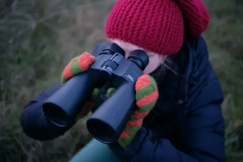 Dziewczyna w czerwonej czapce i rękawiczkach obserwuje niebo przez lornetkę Pentax. Idealna lornetka do obserwacji nieba.