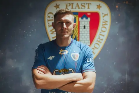 Piast Gliwice ogłasza nowe piast gliwice transfery. Młody piłkarz w niebieskiej koszulce z herbem klubu.