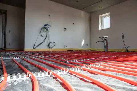 Instalacja podłogówki w garażu w trakcie budowy. Czerwone rurki systemu grzewczego ułożone na folii izolacyjnej.
