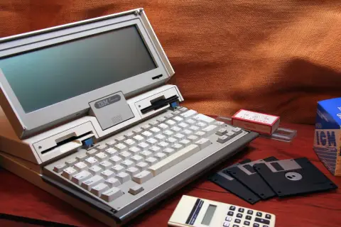 Stary komputer IBM PC Convertible, dyskietki i kalkulator. Kto wymyślił system binarny? To pytanie zadajemy, patrząc na te relikty przeszłości.