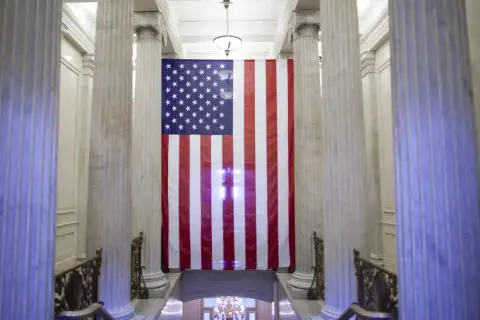Wielka flaga USA wisi między marmurowymi kolumnami. Czy USA to stany zjednoczone? Tak, to symbol tego kraju.