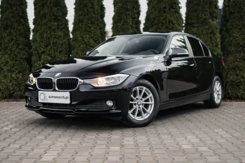 Eleganckie, czarne BMW 318d stoi przed żywopłotem.