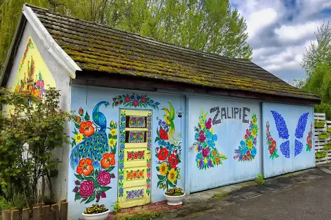 Kolorowy dom w Zalipiu ozdobiony malowidłami kwiatów i pawia. Na ścianie widnieje napis "Zalipie cennik".
