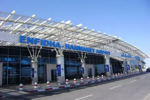 Nowoczesny budynek lotniska Enfidha-Hammamet w Tunezji, z niebieskimi literami nazwy i szklaną fasadą.