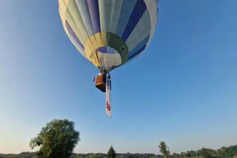 Balon z koszem i banerem unosi się na błękitnym niebie. Może to symbolizować wolność, jak w piosence "99 luftballons znaczenie".