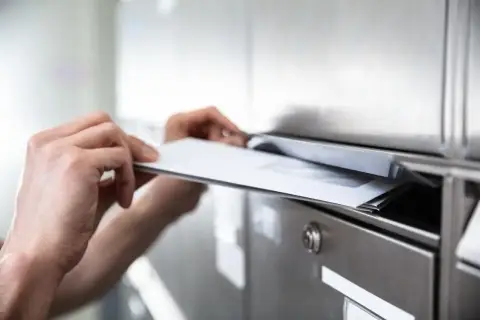 Ręce wkładają koperty do skrzynki pocztowej. To ważna awizacja, która czeka na odbiór.