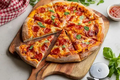 Apetyczna pizza pepperoni z ciągnącym serem i świeżą bazylią, gotowa do podania na drewnianej desce.