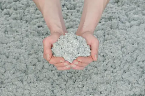 Dłonie trzymają grudkę celulozy, materiału do ocieplenia domu.