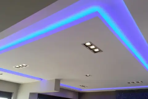 Nowoczesny sufit podwieszany z niebieskim podświetleniem LED. Widać rozmieszczenie punktów świetlnych i taśm LED, tworzących efektowną ramę.
