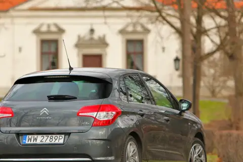 Szary Citroen C4 1.6 HDi zaparkowany przed zabytkowym budynkiem.