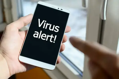 Dłoń trzyma smartfon z napisem "Virus alert!". Czas zainstalować antywirus na telefon.