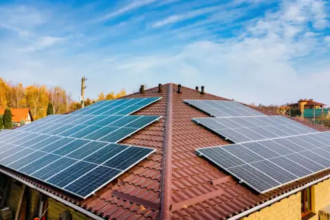Dach pokryty brązową dachówką z zainstalowanymi panelami fotowoltaicznymi. Widać kilka rzędów ogniw monokrystalicznych, które zbierają energię słoneczną.