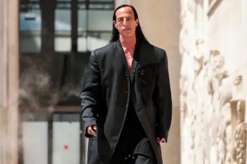 Rick Owens, w charakterystycznym czarnym płaszczu, idzie pewnym krokiem.