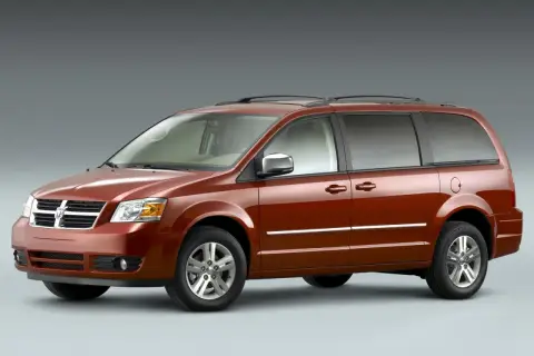 Pomarańczowy Dodge Grand Caravan z chromowanymi listwami i relingami dachowymi, gotowy na rodzinną podróż.
