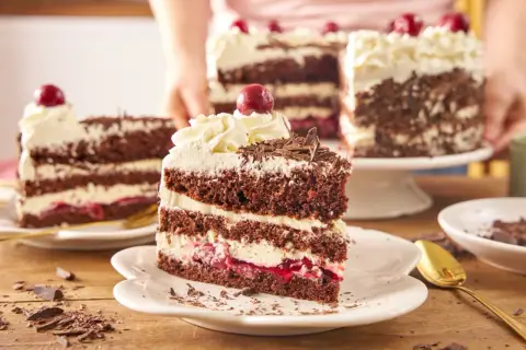 Pyszny tort szwarcwaldzki z mascarpone, przełożony kremem i wiśniami, ozdobiony czekoladowymi wiórkami i wisienką.