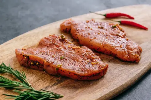 Dwa kawałki indyka w marynacie z gorczycą i pieprzem, obok gałązka rozmarynu i dwa czerwone chili.