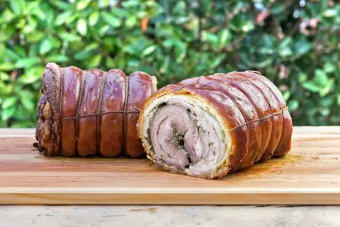 Dwa pieczone kawałki porchetta, zawinięte w skórkę i sznurki, leżą na desce. To pyszne danie, które warto poznać!