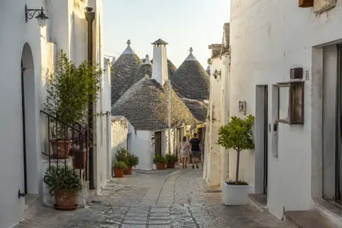 Ruelle pavée bordée de maisons blanches aux toits coniques typiques des Pouilles à éviter, avec un couple se promenant.