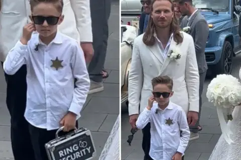 Chłopiec w okularach przeciwsłonecznych, z odznaką i walizeczką "Ring Security", towarzyszy parze młodej.