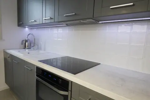 Nowoczesna kuchnia z szarymi frontami i białymi kafelkami. Blat o wysokości 95cm, z płytą indukcyjną i zlewozmywakiem.