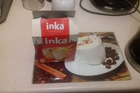 Pudełko Inki i filiżanka kawy na podkładce. Czy kawa Inka jest dla dzieci? To napój zbożowy, idealny dla całej rodziny.