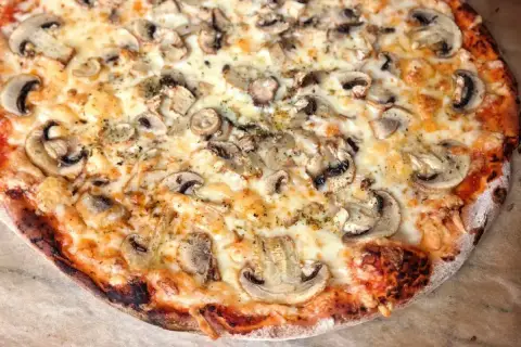 Pyszna pizza capricciosa z pieczarkami i ciągnącym się serem, idealna na wieczór z przyjaciółmi.