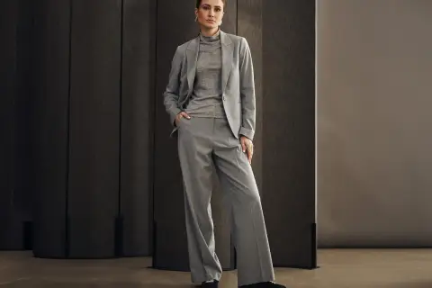 Elegancka kobieta w szarym garniturze, idealnym na wesele w spodniach. Stylowa i pewna siebie.