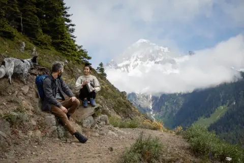 Para, pies i pies odpoczywają na szlaku, podziwiając majestatyczne góry. To właśnie jest **trekking co to** – przygoda i bliskość natury.