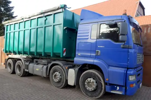 Blauer LKW mit großem grünen Container. Die Bedeutung eines solchen LKW ist der Transport von Schüttgut oder Abfall.