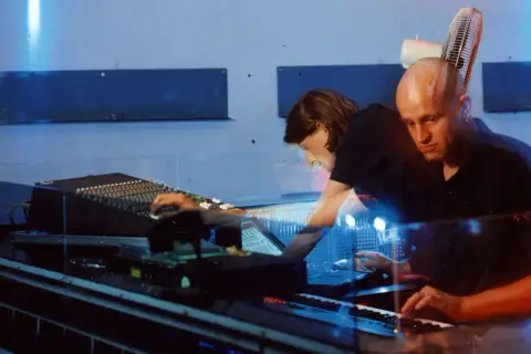 Robert Henke und Kollegin im Studio, umgeben von blauem Licht und Musik-Equipment.