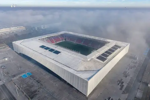 Nowy stadion Odra Opole wyłania się z mgły. Nowoczesna bryła z panelami słonecznymi i czerwonymi trybunami.